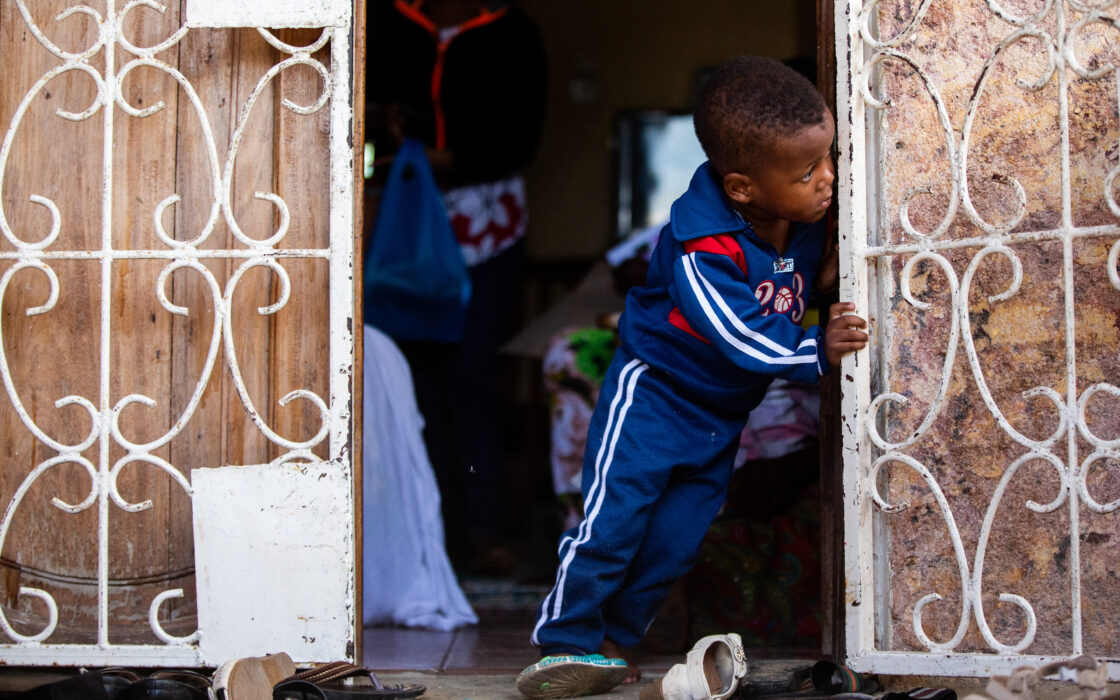 Child peeking out of the family home while leaning on the door