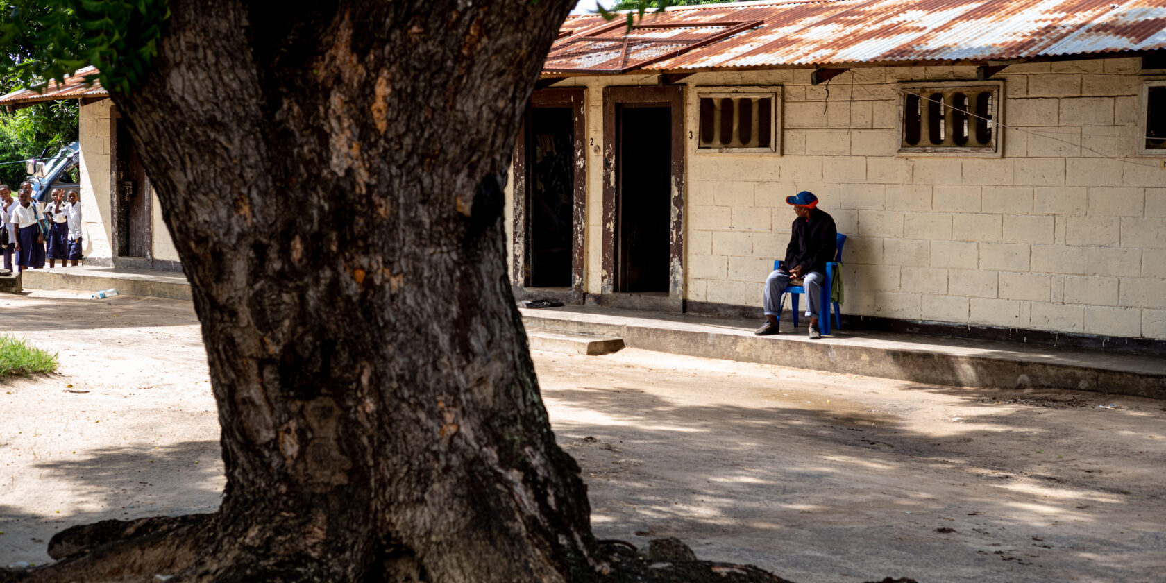 An elderly man relaxing in a chair, with some children in the distance